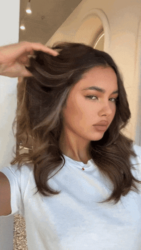a woman wearing a white t-shirt is holding her hair