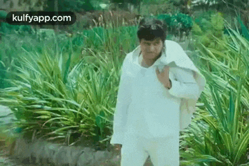 a man in a white shirt and white pants is standing in a park .