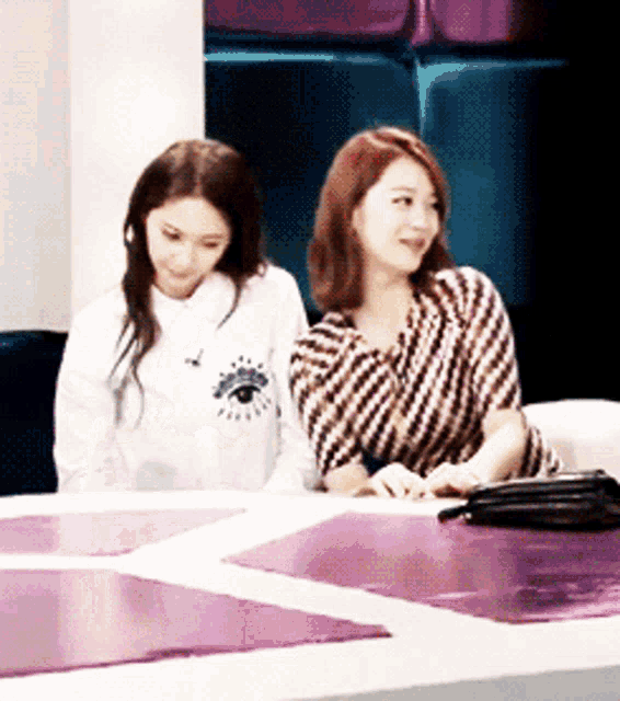 two women are sitting at a table with one wearing a shirt with an eye on the front