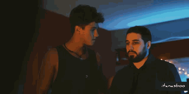 two men are standing next to each other in a dark room with a blue light behind them that says ifanasboo
