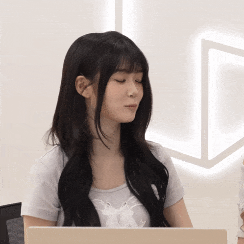 a woman with long black hair is sitting in front of a laptop with her eyes closed