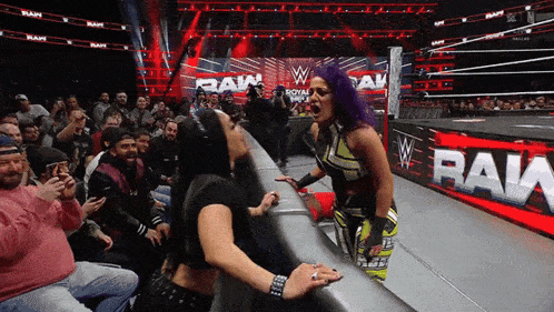 two women wrestling in front of a crowd with the word raw on the wall