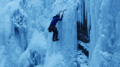a person is climbing up a frozen waterfall with a hammer