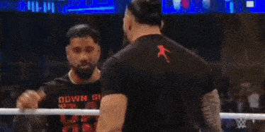 a man in a black shirt is standing in a wrestling ring .