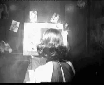 a black and white photo of a woman in a dark room looking at a television .
