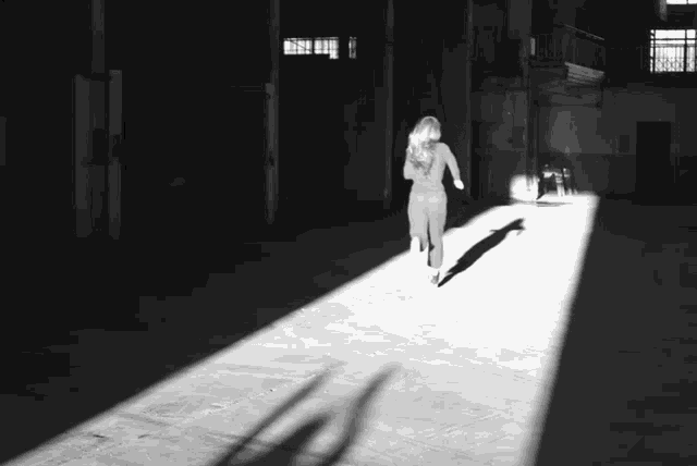 a naked woman is running through a dark room with a shadow on the floor