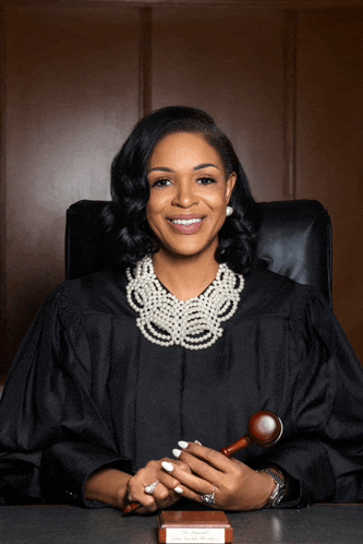 a woman in a judge 's robe is smiling while holding a gavel and a book that says " justice "