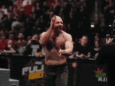 a bald man with a beard and a white tank top looks at the camera