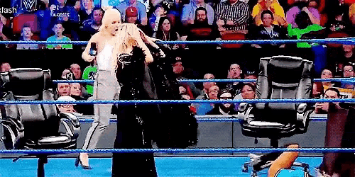 two women are standing in a wrestling ring with chairs in front of a crowd .