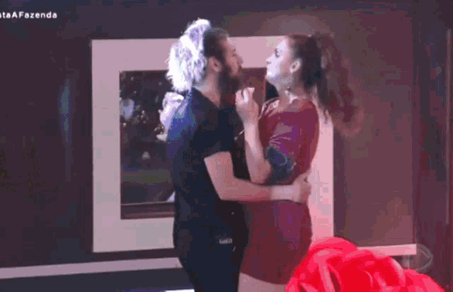 a man and a woman are dancing in front of a wall with the word fazenda written on it .