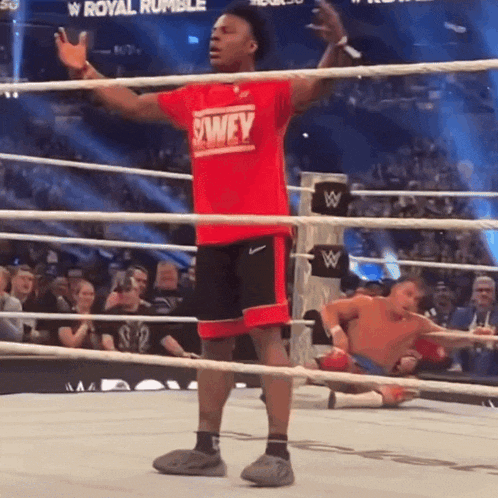 a wrestler wearing a red shirt that says swey stands in a ring