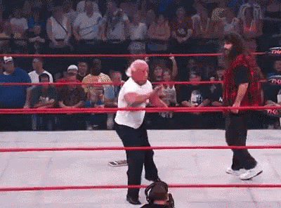 a man is dancing in a wrestling ring while another man watches .