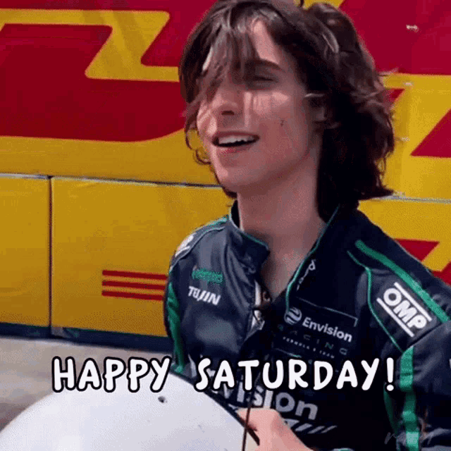 a young man in a racing jacket is smiling and says happy saturday