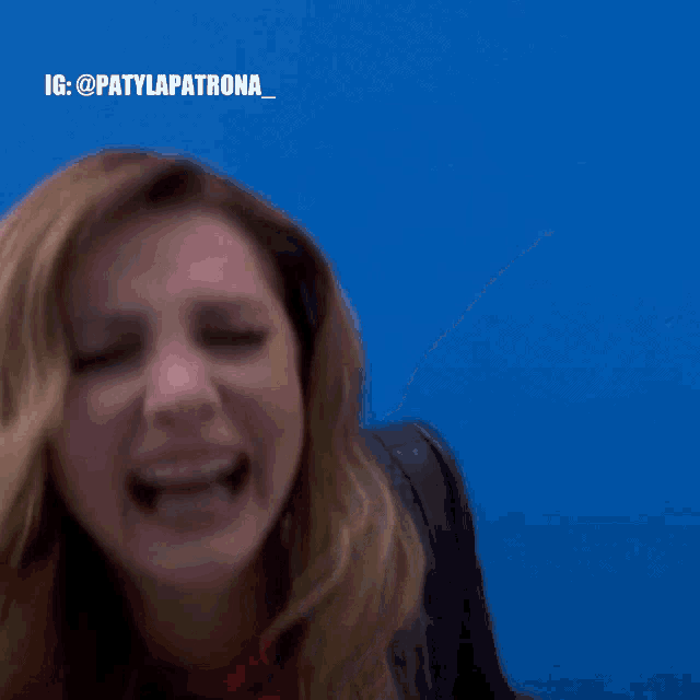 a woman is laughing with her mouth open and a blue background behind her