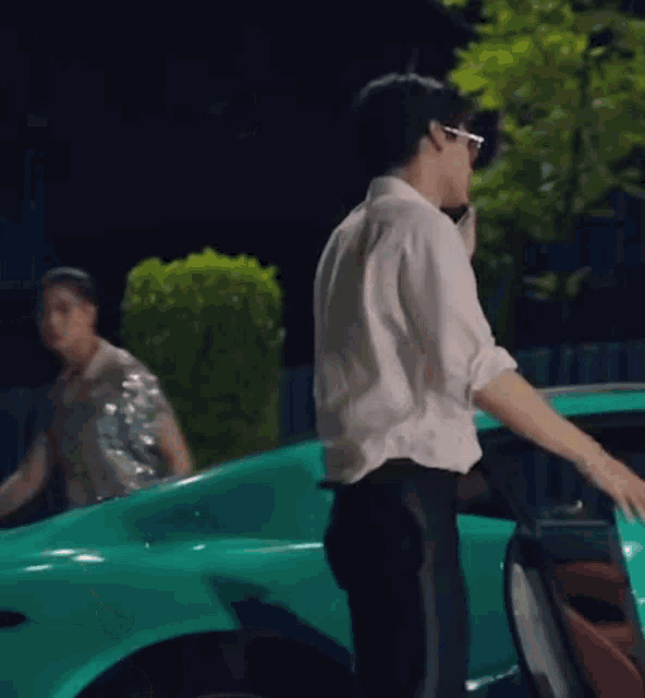 a man in a white shirt and black pants is getting out of a green sports car .