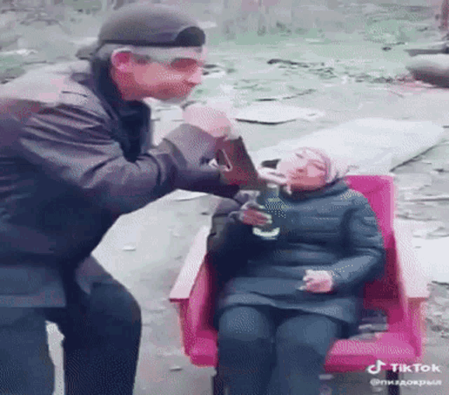 a man is standing next to a woman in a pink chair holding a bottle of beer .