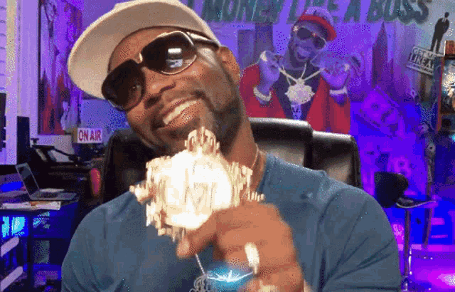 a man wearing sunglasses and a hat is holding a stack of money in front of a poster that says money like a boss