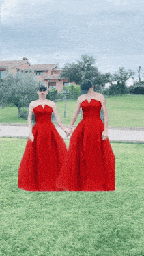 two women in red dresses are holding hands in a grassy field