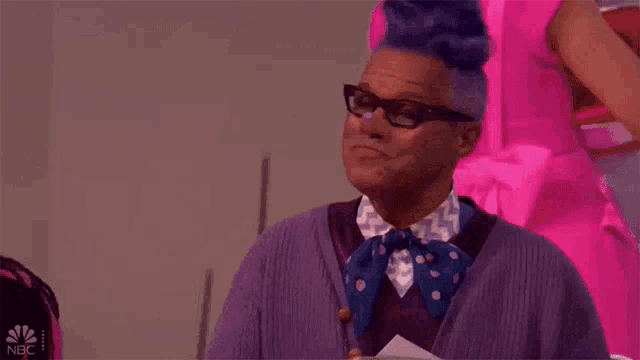 a man with purple hair and glasses is wearing a purple sweater and a blue bow tie ..