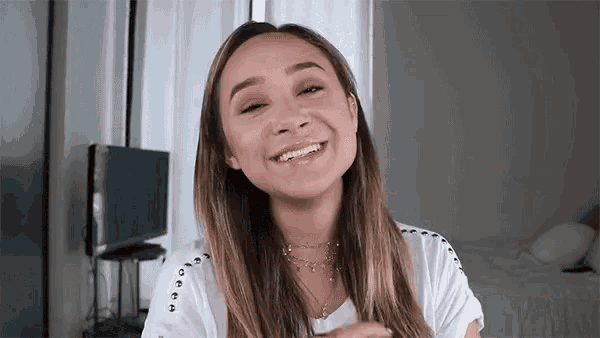 a woman is smiling and looking at the camera while wearing a white shirt and necklace .