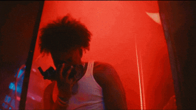 a man in a white tank top is singing into a microphone in a dark room .