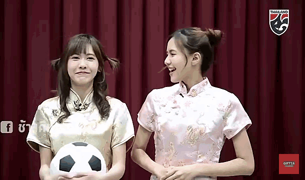 two girls holding a soccer ball in front of a red curtain with a thailand logo on it