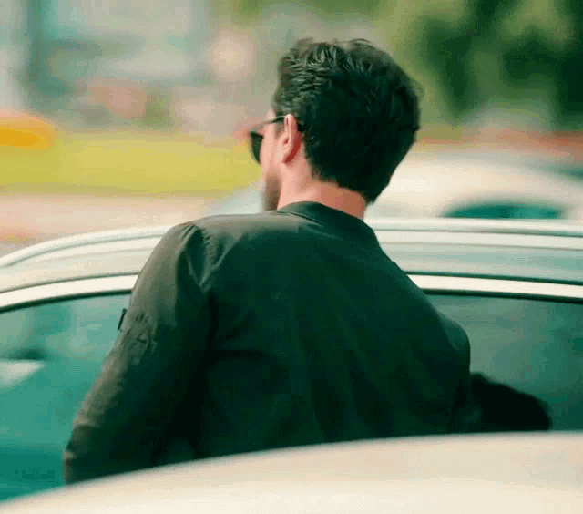 a man wearing sunglasses and a black jacket looks out of a car window