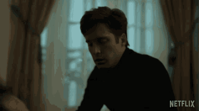 a man in a black turtleneck sits in front of a window with a netflix logo on the bottom right
