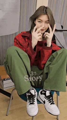 a woman wearing a red jacket and green pants is sitting on a chair with the word story on the back