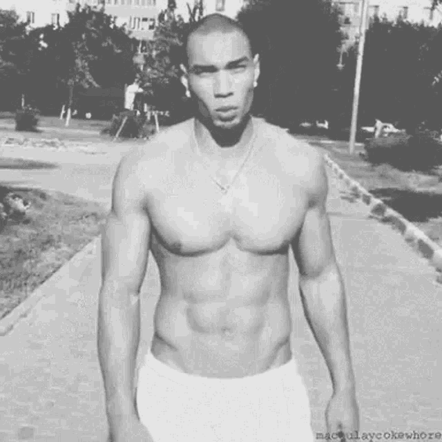 a shirtless man is standing on a sidewalk in a black and white photo .