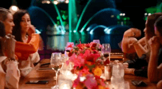 a group of people are sitting at a table with a vase of flowers in front of them .
