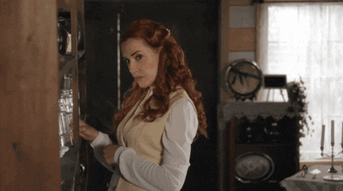 a woman with red hair is standing in a room with a clock on the wall