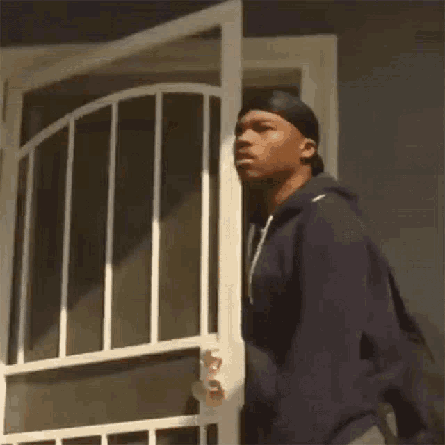 a man in a black hoodie is standing in front of a white screen door .