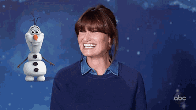 a woman in a blue sweater is smiling in front of an animated snowman from abc