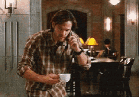 a man talking on a cell phone while holding a cup of coffee .