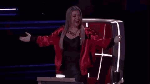a woman in a red jacket is standing in front of a podium with her arms outstretched on a stage .