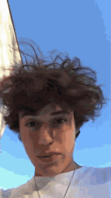 a young man with curly hair is wearing a white shirt and a white necklace .
