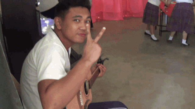 a young man giving a peace sign while holding an acoustic guitar