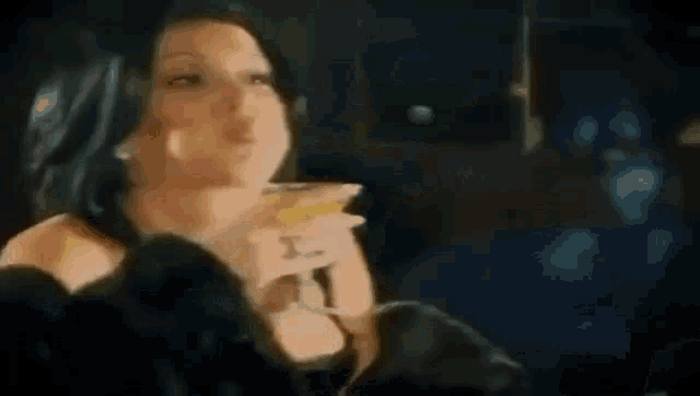 a woman is smoking a cigarette in a dark room while holding a drink .