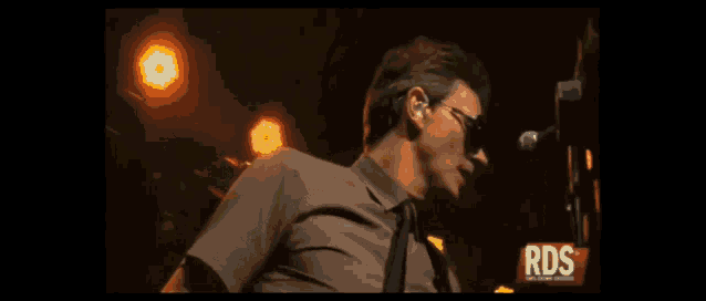 a man in a suit and tie is playing a guitar in front of a sign that says rds