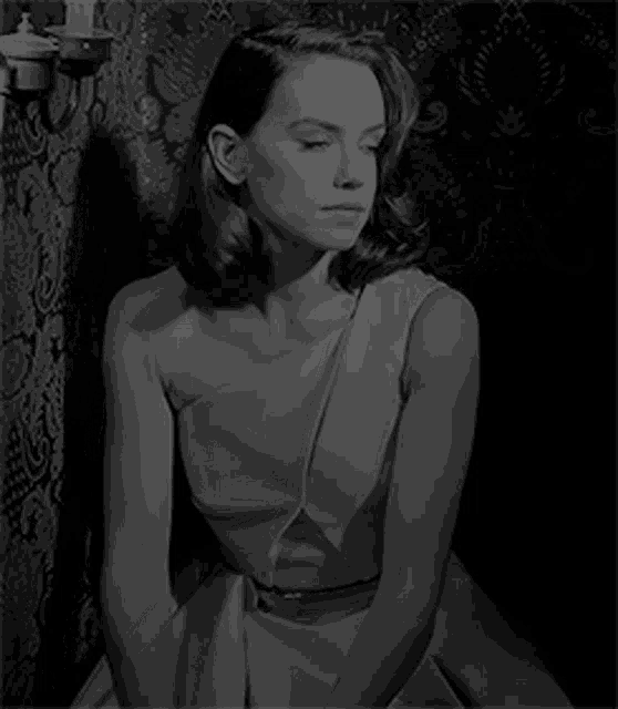 a black and white photo of a woman in a dress sitting on a chair .