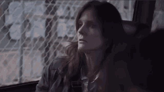 a woman with long hair is sitting in a car with a fence in the background .