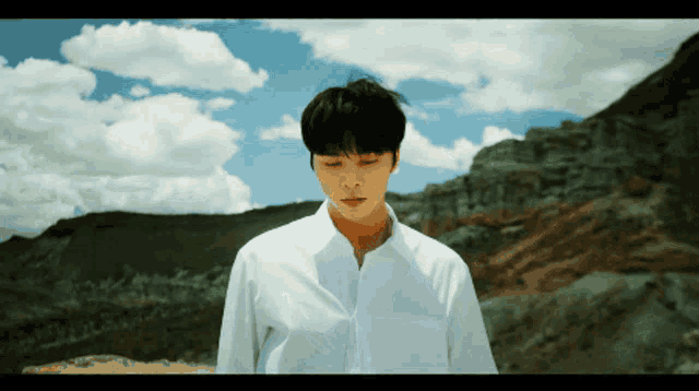 a man in a white shirt is standing in front of mountains