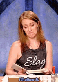 a woman wearing a tank top that says slay is sitting at a table