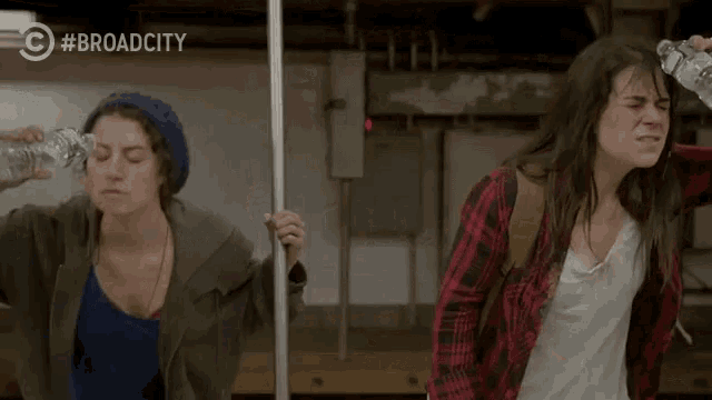 two women drinking water on a subway train with a #broadcity logo behind them