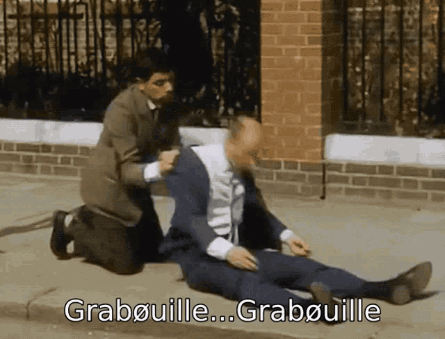 a man in a suit is laying on the ground while another man kneels next to him