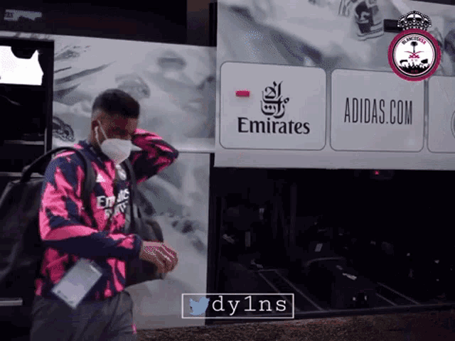 a man wearing a mask is walking in front of an emirates bus