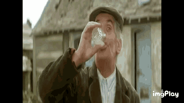 a man is drinking from a glass in front of a house .