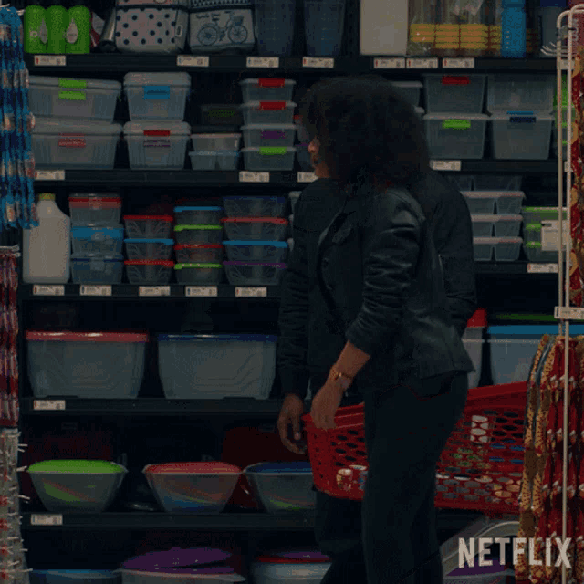 a woman in a black jacket stands in front of a shelf with netflix written on it