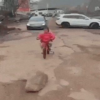 a little girl is pushing a bicycle on a dirt road in front of a car .